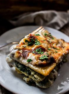 a white plate topped with lasagna covered in cheese and spinach on top of a wooden table