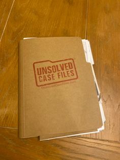 an unsolved case files book sitting on top of a wooden table next to a pair of scissors