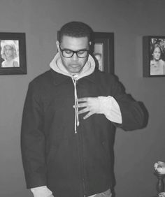 a man wearing glasses and a hoodie standing in front of pictures on the wall