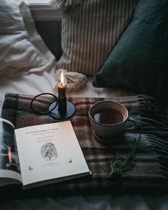 an open book with a candle and cup on a bed