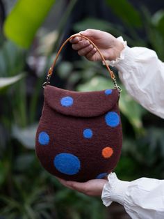 a hand holding a brown and blue purse with polka dots on the outside, in front of some plants