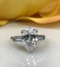 a diamond ring with three baguets on the side and a yellow rose in the background