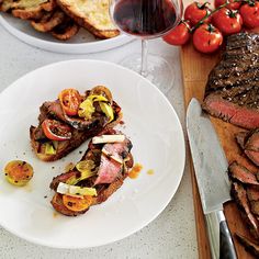 steak, bread and tomatoes on a white plate next to a glass of red wine