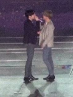 two young men standing next to each other on top of a ice skating rink at night