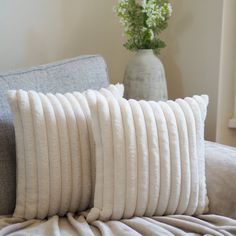 two pillows sitting on top of a couch next to a vase with flowers in it