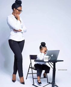 a woman standing in front of a laptop computer next to another woman sitting at a desk