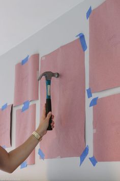 a person holding a hammer in front of pink sticky notes on a wall with blue tape