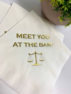 two napkins with the words meet you at the bar on them next to a potted plant