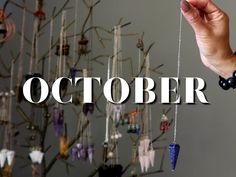 a hand holding a string with the word october hanging from it in front of a tree