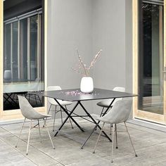 a glass table with four chairs and a vase filled with flowers on top of it