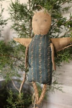 an old cloth doll hanging from a tree with green needles and branches in the background