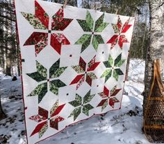 a quilt hanging from a tree in the snow next to a sled and basket