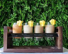 four glasses filled with different types of drinks on a wooden tray in front of a green wall