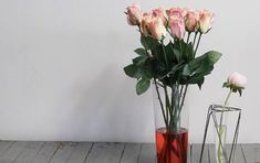 a vase filled with pink roses sitting on top of a wooden floor next to a glass vase