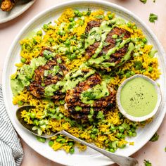 a white plate topped with chicken and rice covered in guacamole sauce next to a bowl of salsa