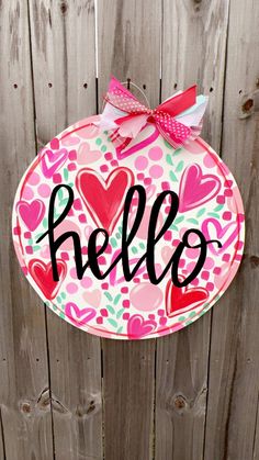 a paper plate with the word hello written on it and hearts painted on it, hanging from a wooden fence