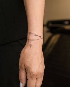 a woman's hand with a tiny cross tattoo on her left wrist, and a thin band around the wrist