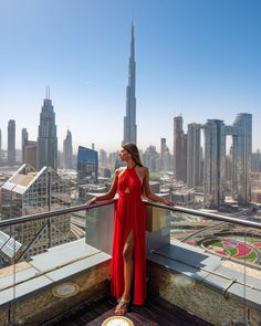 a woman in a red dress is standing on a balcony overlooking the cityscape