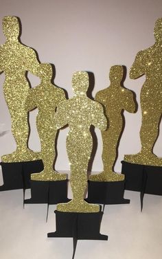 three gold and black paper cutouts are standing in the shape of people with arms around each other