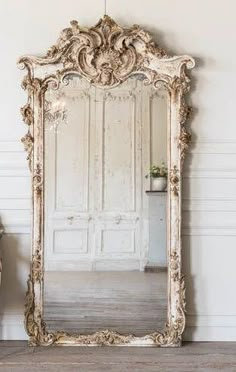 an ornate mirror sitting on top of a wooden floor next to a vase and potted plant