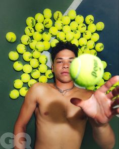 a shirtless man holding a tennis ball in front of a bunch of tennis balls