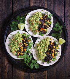 three white plates topped with black beans, guacamole and cilantro