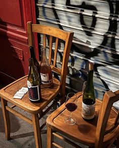 two wooden chairs with wine bottles and glasses sitting on them in front of a graffiti covered wall