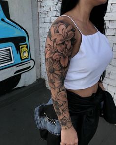 a woman with a flower tattoo on her arm is walking down the street in front of a brick wall