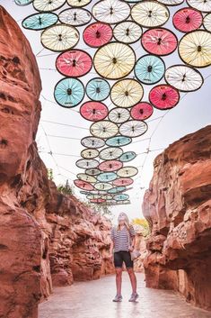 a woman is standing under colorful umbrellas hanging from the ceiling