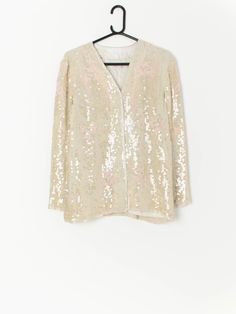 Vintage beaded sequin jacket in ivory and pink. This jacket features a hook and loop chest closure and a smooth lining. The jackets pattern features transparent sequins on a ivory material and an abstract beaded baby pink pattern. Made from a synthetic material. This jacket is the perfect party piece! Our recommended size: Small / Medium Label says: No size label Condition: Very good*: has a small part of thread with slight discolouration on the front right side, and what looks like a mark from Summer Sequined Long Sleeve Outerwear, Sequined Long Sleeve Summer Outerwear, White Sequined Long Sleeve Outerwear, Glamorous Pink Sequined Outerwear, Pink Sequined Outerwear For Spring, White Sequined Outerwear For Party, Fall Wedding Outerwear With Sequins, Glamorous Spring Wedding Outerwear, Summer Long Sleeve Embellished Outerwear