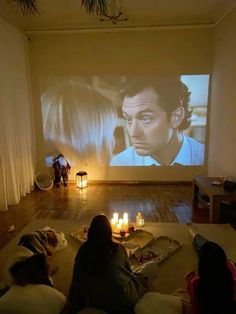 people sitting on the floor in front of a projector screen with candles lit up