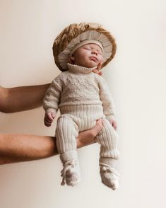 a person holding a baby wearing a knitted hat and diaper on it's head