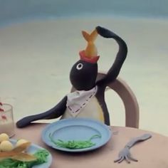 a penguin sitting at a table with food and drink