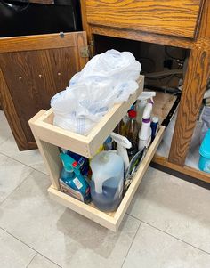 an open cabinet filled with bottles and other household cleaning products on the floor next to a sink