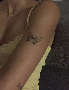 a woman with a butterfly tattoo on her arm, sitting in front of a couch