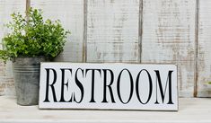 a sign that says restroom on it next to a potted plant