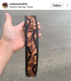 a hand holding up a brown and black leather belt with intricate designs on the side