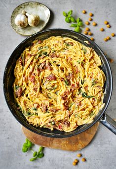 a skillet filled with pasta and vegetables on top of a wooden cutting board next to garlic