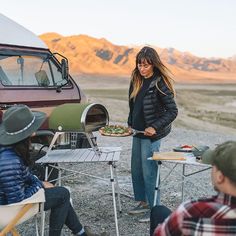 a group of people sitting around a camper with food in front of them on the ground