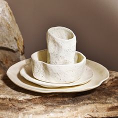 a stack of three white dishes sitting on top of a wooden table next to a rock