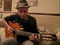 a man sitting on a couch playing an acoustic guitar with a hat on his head