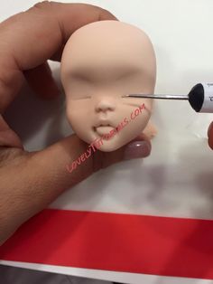 a hand holding a needle with a fake baby head on it