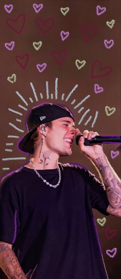 a man with tattoos holding a microphone in front of hearts drawn on the wall behind him