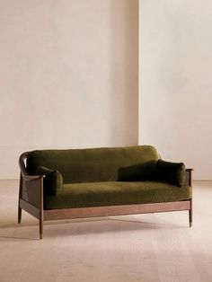 a green couch sitting on top of a hard wood floor next to a white wall