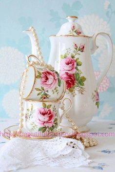 two porcelain teapots with pink roses on them sitting next to a lace doily