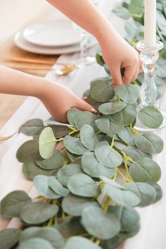 a woman is decorating a table with greenery