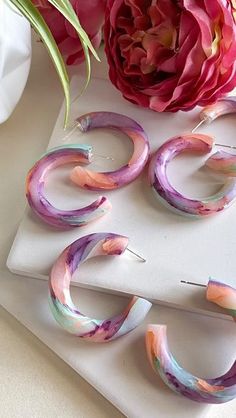 three pairs of painted hoop earrings sitting on top of a table next to a pink flower