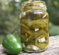 pickles and peppers are in a jar on a table next to a green pepper