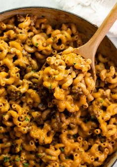 macaroni and cheese is being stirred with a wooden spoon in a skillet