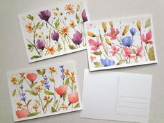 three cards with flowers painted on them are next to an envelope and some white paper